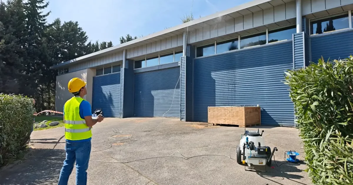 Télépilote en gilet haute visibilité pilotant un drone devant les hangars du campus TELEPILOTE de Marcq pendant l'évaluation STS