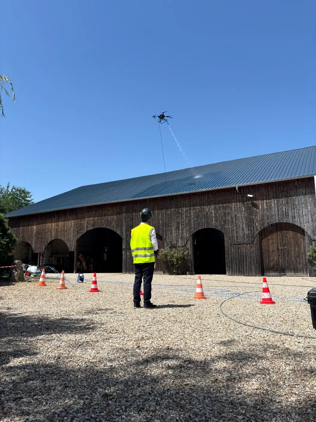 Drone en vol au-dessus des hangars du campus, télépilote au sol et cônes délimitant la zone pendant l'évaluation STS-01