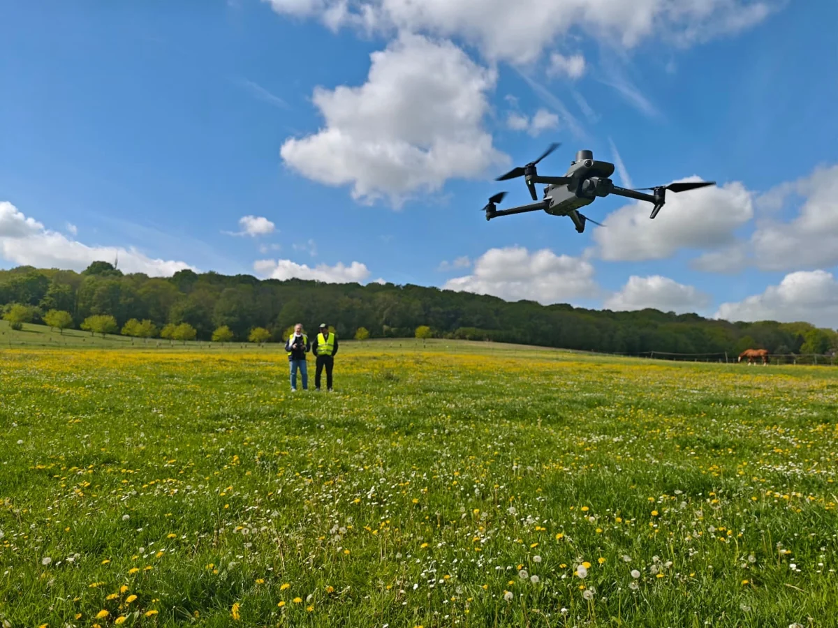 Drone en vol et deux télépilotes en formation sur le terrain TELEPILOTE